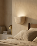 Wabi-Sabi Travertine Wall Sconce in luxury residential bedroom, warm plaster walls, golden hour light