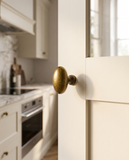 Floral Antique Brass Cabinet Knob — hero installed view, cream Shaker kitchen cabinet door, warm vintage brass glow