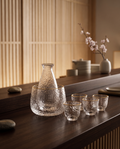 Glass Sake and Bar Serving Set, 6-Piece — hero arrangement, minimalist Japanese dark wood bar, clear glassware in warm evening light