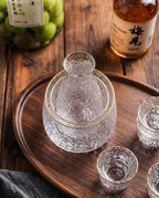 Glass Sake and Bar Serving Set, 6-Piece — alternate top-down angle, dark wood surface, glass carafe and glasses