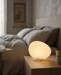 Pebble-Shaped LED Bedside Night Light — hero on bedside table, Japandi bedroom, soft warm glow