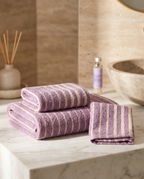 Lavender Striped Combed Cotton Towel Set — full set of bath and hand towels folded together for scale, marble counter, warm light