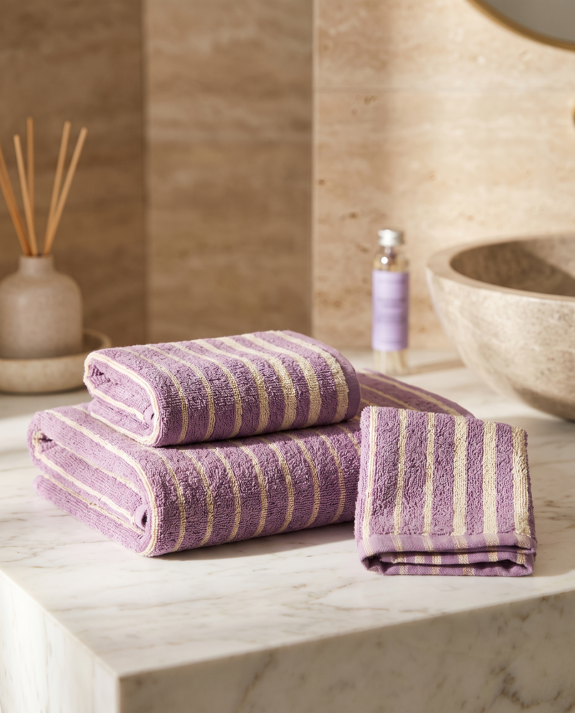 Lavender Striped Combed Cotton Towel Set — full set of bath and hand towels folded together for scale, marble counter, warm light