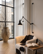 Black Iron Swing Arm Wall Light, Adjustable — beside a reading chair in a cozy living room, arm swung out with warm reading glow
