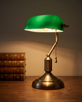 Green Shade Banker's Desk Lamp, Antique Brass LED — on a warm walnut study desk with leather-bound books and a focused pool of light