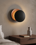 Round Moon Eclipse LED Wall Sconce, Copper — Black & Copper hero, mounted above nightstand in modern bedroom