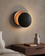 Round Moon Eclipse LED Wall Sconce, Copper — Black & Copper hero, mounted above nightstand in modern bedroom